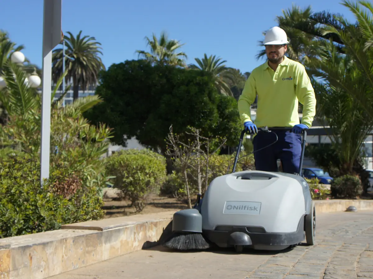 Trabajador de CleanVip operando una barredora entre los jardines de una instalación