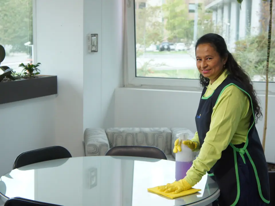 Trabajadora de CleanVip limpiando la mesa de vidrio de una sala de reunión