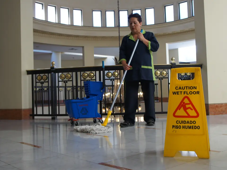 Trabajador de CleanVip pasando mopa en un hall amplio, con señalización de piso húmedo